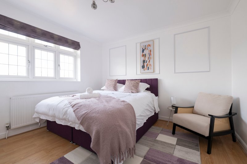 Bright bedroom with double bed, purple headboard, wooden floor and armchair by window