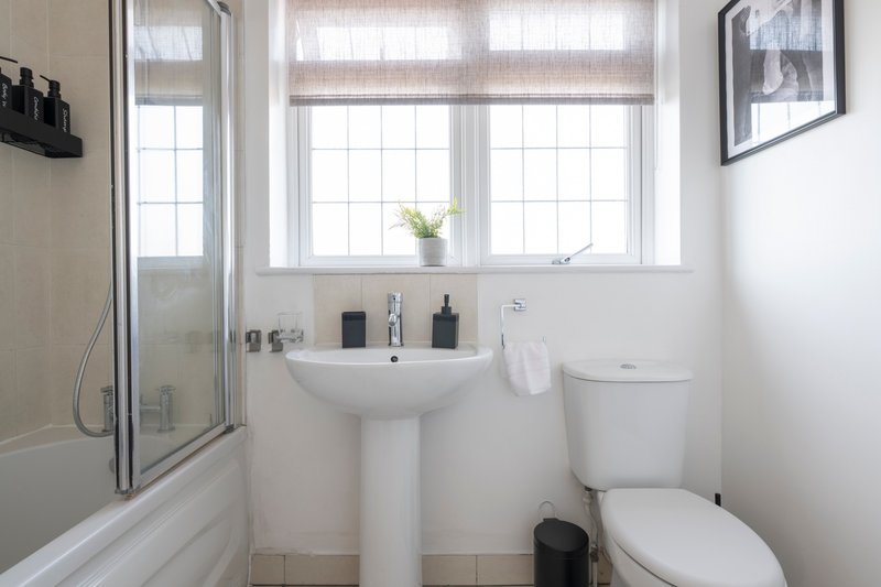 Bright bathroom with pedestal sink, toilet, shower enclosure and frosted window