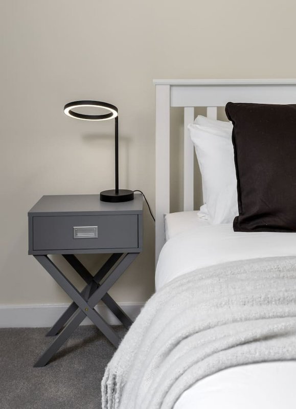 Bedroom bedside table with lamp, white pillows and black cushion on bed