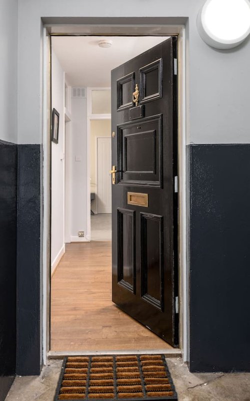 Open black front door with brass hardware, white-framed doorway, wood flooring and brown doormat visible