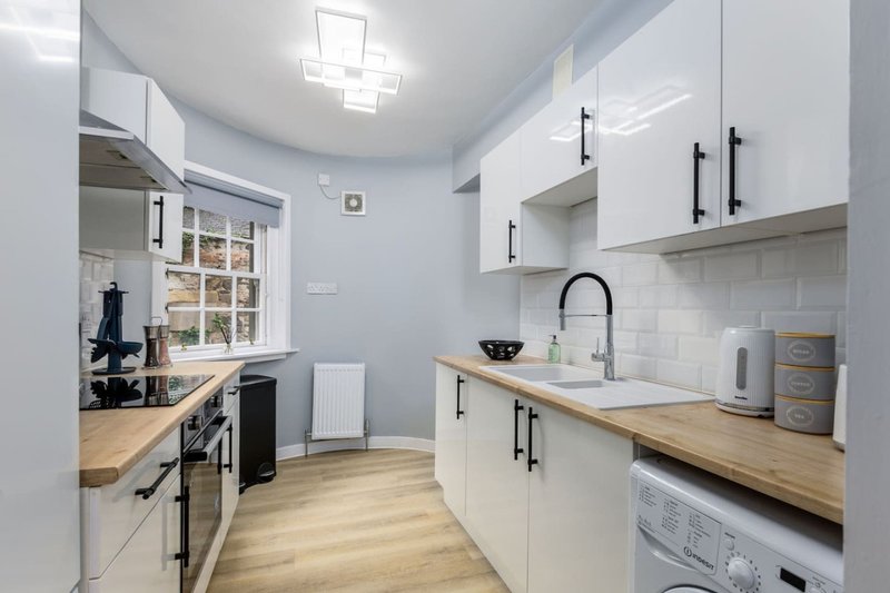 Modern galley kitchen with white cabinetry, wooden worktops, stainless steel appliances and subway tile backsplash