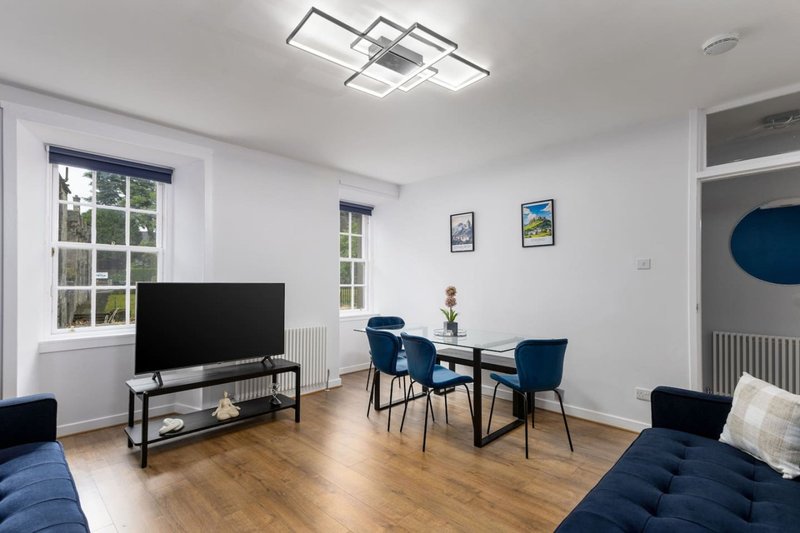 Bright living room with TV, dining table, blue chairs and wooden flooring