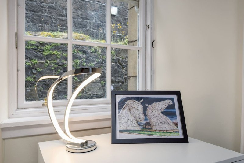 White desk with curved lamp, framed artwork, and window overlooking garden