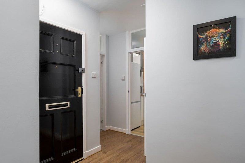 Hallway with black front door, white walls, wooden floor and framed artwork