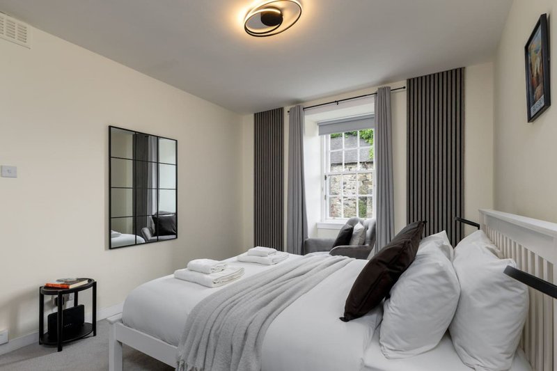 Modern bedroom with double bed, white bedding, black cushions, window with grey curtains
