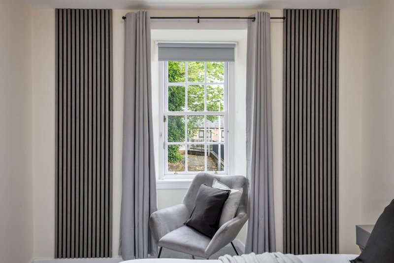 Bedroom with grey armchair by window, floor-to-ceiling curtains, natural light