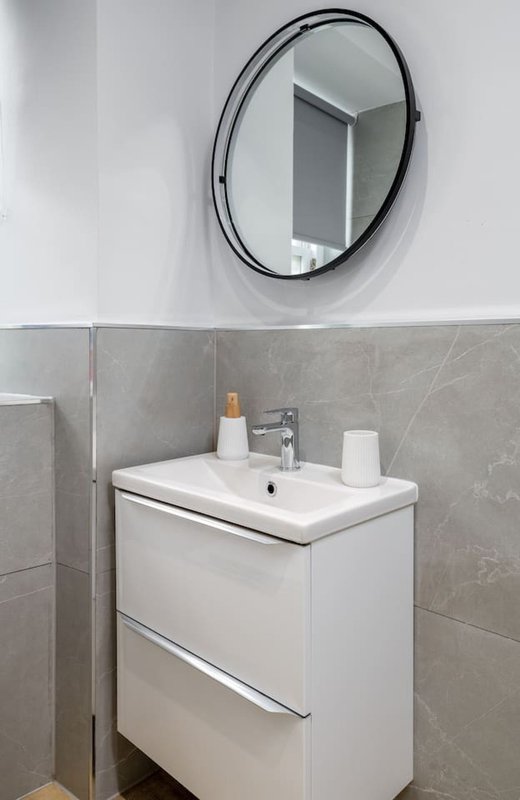 Modern bathroom with round mirror, white vanity sink and grey tile walls
