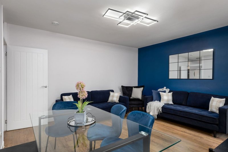 Modern living room with dark blue sofa, glass dining table, blue accent wall and white door