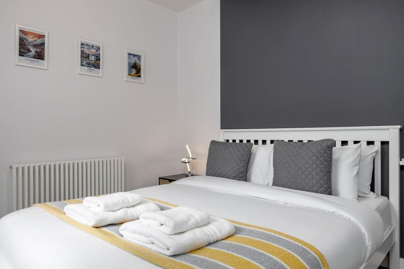 Modern bedroom with double bed, white pillows, grey headboard and wall art