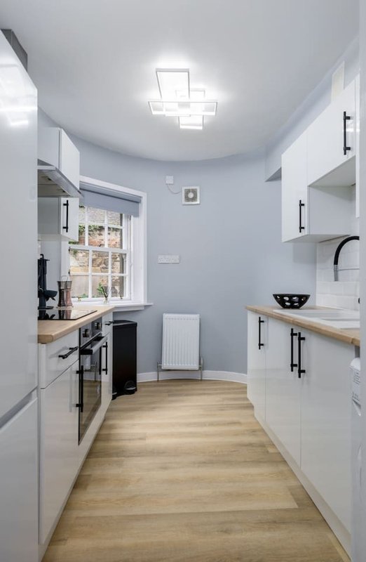 Modern galley kitchen with white cabinetry, wooden worktops, and geometric ceiling light