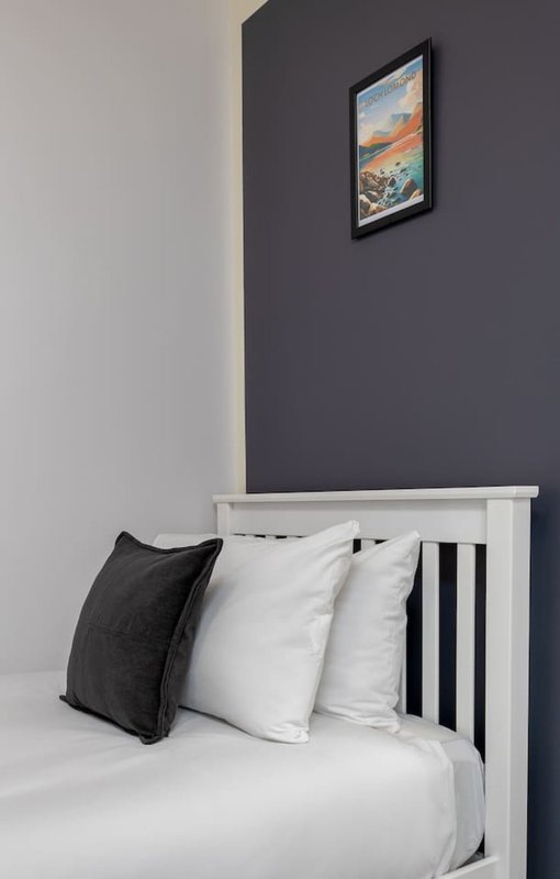 Modern bedroom with white bed frame, black and white pillows, dark accent wall, framed artwork