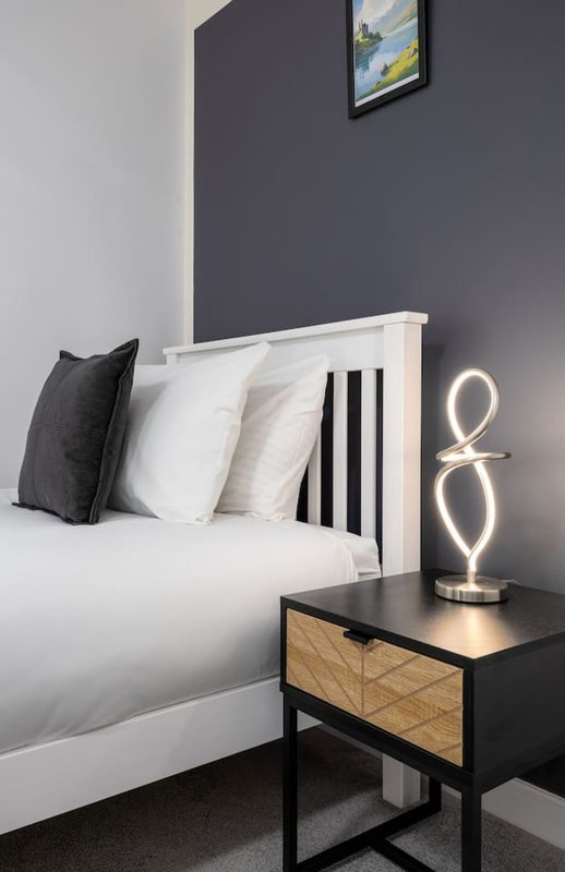 Modern bedroom with white bed, black and white pillows, neon light, and dark nightstand