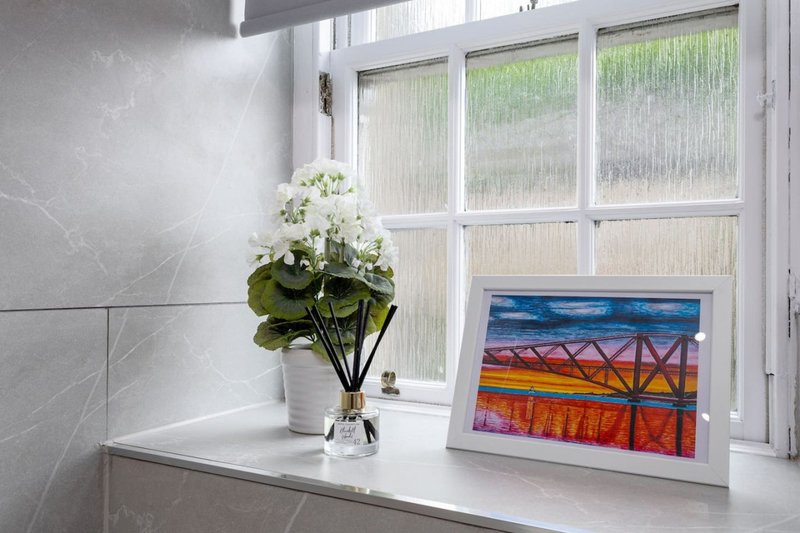Bright windowsill with white flowers in vase, framed landscape artwork, and marble-effect wall