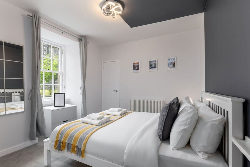 Bright modern bedroom with double bed, white furniture, grey accents and window with garden view