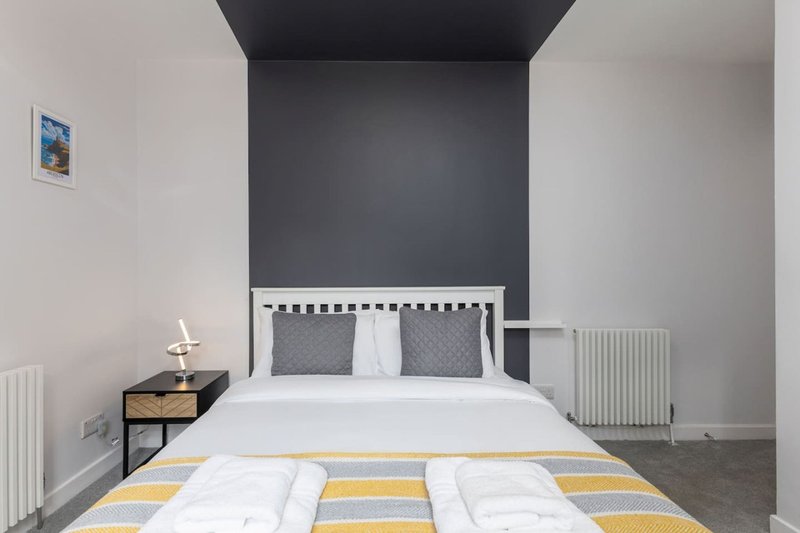 Modern bedroom with double bed, dark headboard, white bedding and yellow striped throw