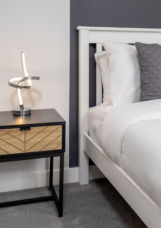 Modern bedroom with white bed, grey headboard, black nightstand with lamp