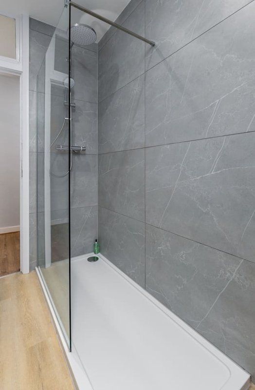 Modern bathroom with walk-in shower, grey tile walls, and white base tray