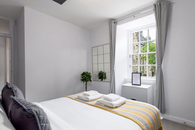 Bright bedroom with white bed, yellow throw, window with garden view, and potted plant