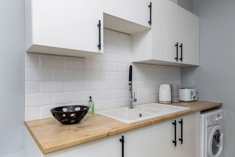Modern kitchen with white cabinetry, wooden countertop, white subway tile backsplash and integrated washing machine