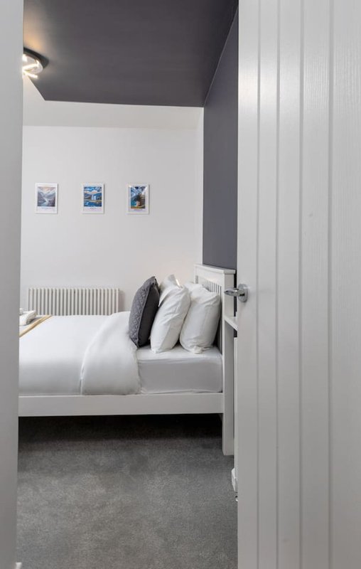 Modern bedroom with white bed, dark pillows, white ceiling, and three framed artworks on wall