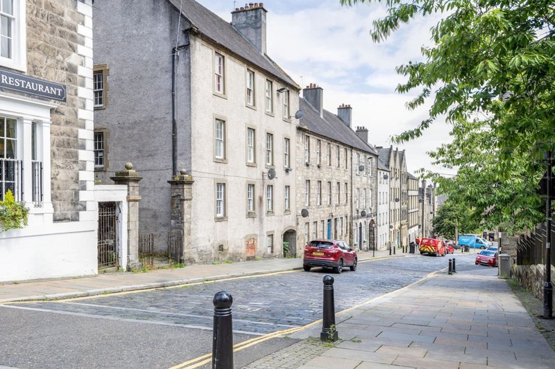 Stone tenement buildings lining a quiet street with parked cars and bollards