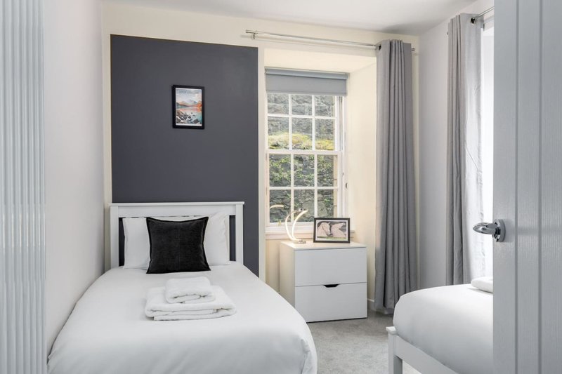 Modern bedroom with single bed, dark accent wall, window seat and grey curtains