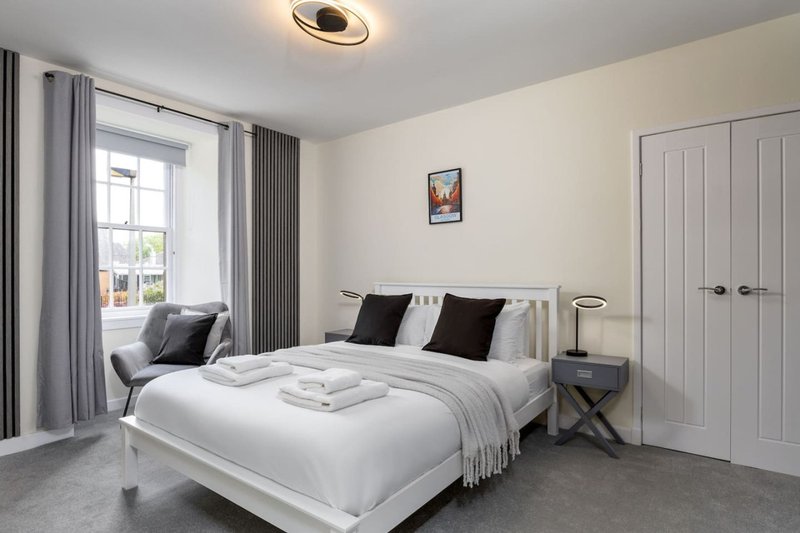 Modern bedroom with white bed, black pillows, grey curtains, window and ceiling light