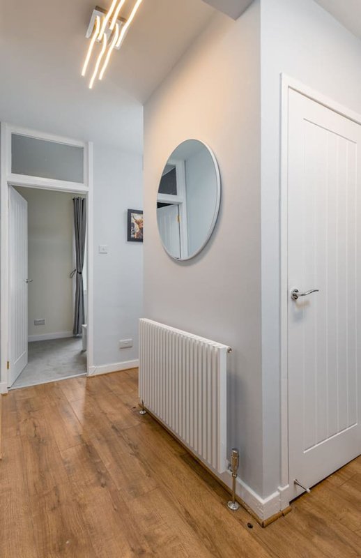 Modern hallway with wooden flooring, white walls, round mirror, radiator and pendant lighting