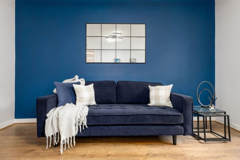 Modern living room with dark blue sofa, geometric wall mirror, wooden floor and side table