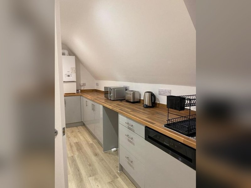 Compact kitchen with white cabinets, wooden worktops, black oven and kettle under sloped ceiling