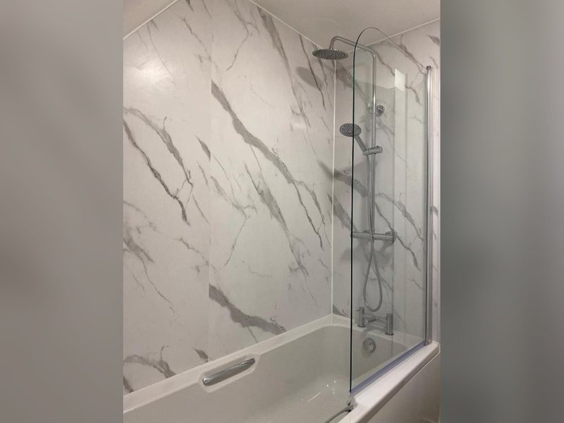 Modern bathroom with marble-effect wall tiles, glass shower enclosure and white bathtub