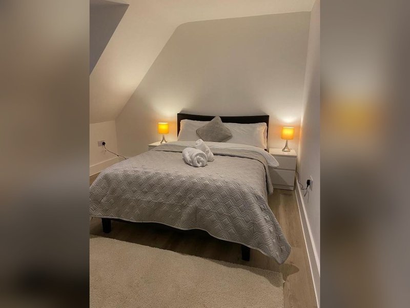 Attic bedroom with double bed, gray bedding, black headboard, and two bedside lamps