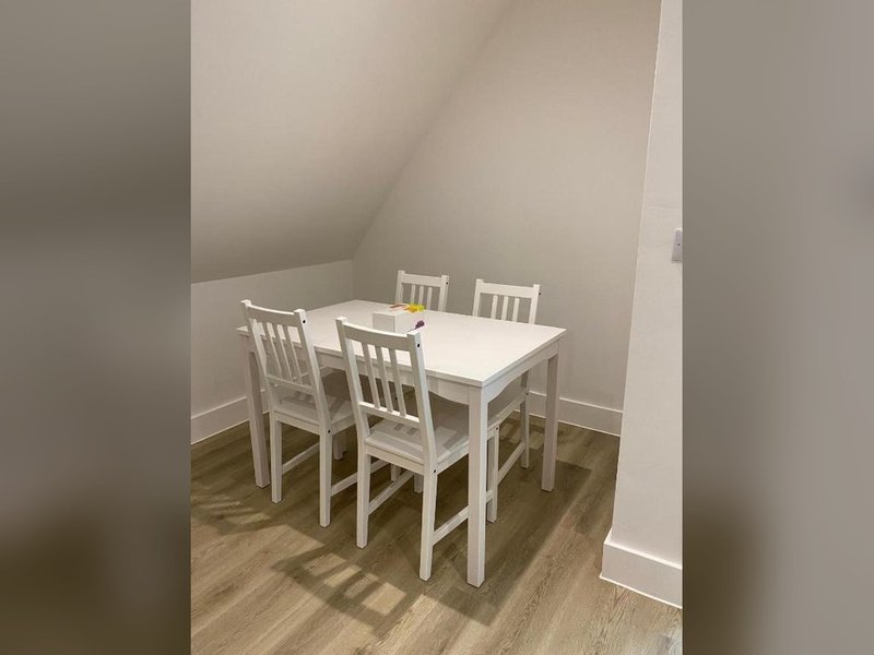 Small dining area with white table and four white chairs on wooden floor