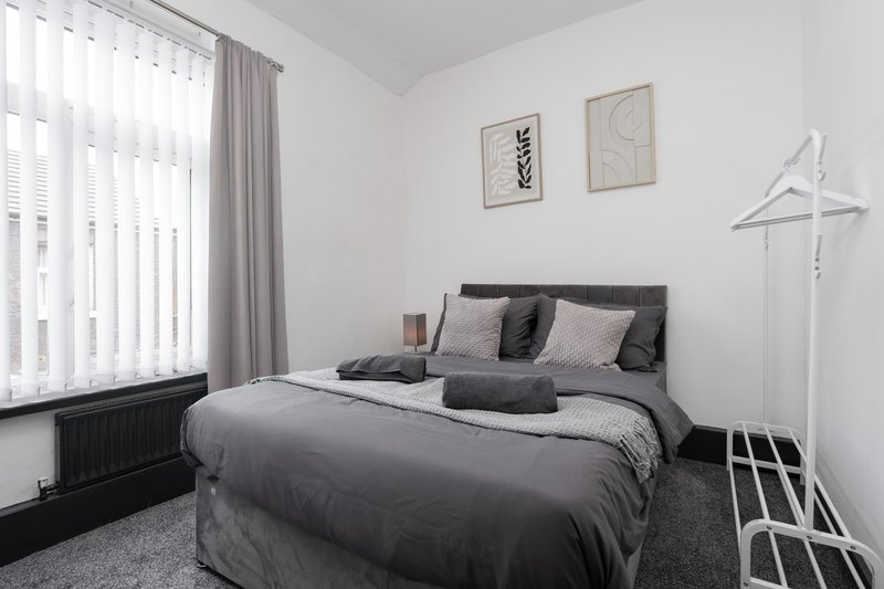 Modern bedroom with double bed, grey bedding, wall art, window with curtains and clothes rack