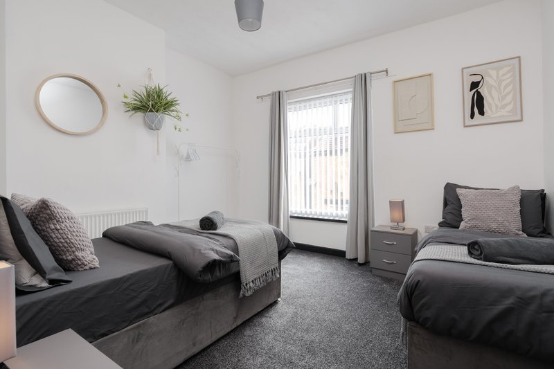 Bright bedroom with two single beds, grey bedding, round mirror, hanging plant and framed wall art