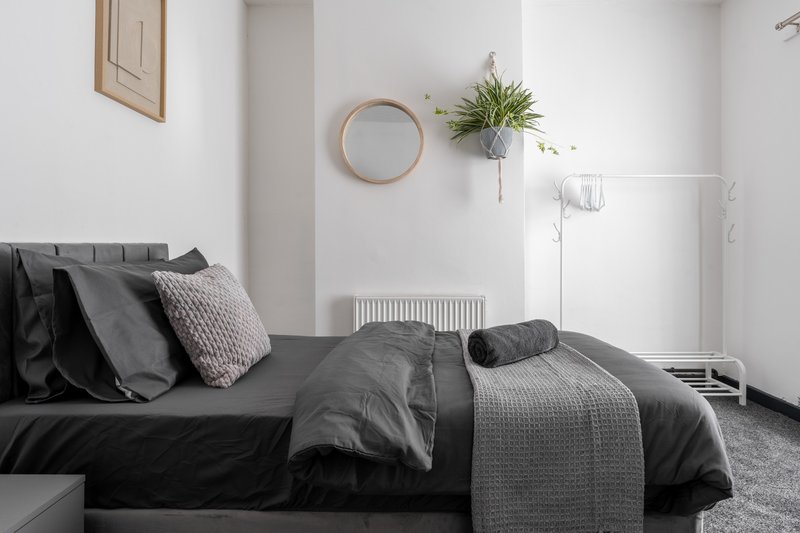 Modern bedroom with dark double bed, grey bedding, wall-mounted mirror and potted plant