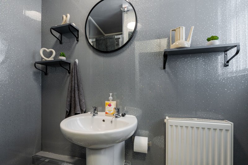Modern bathroom with pedestal sink, round mirror, black shelving and radiator