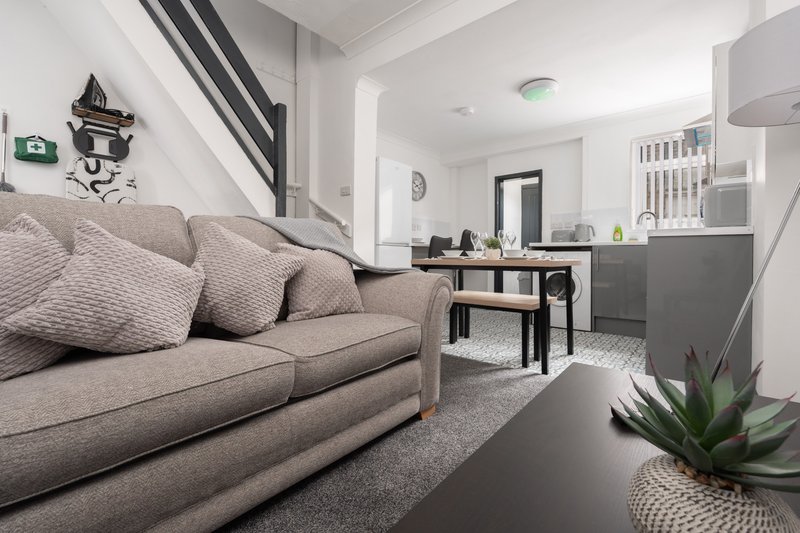 Open-plan living area with grey sofa, kitchen, dining table, and staircase