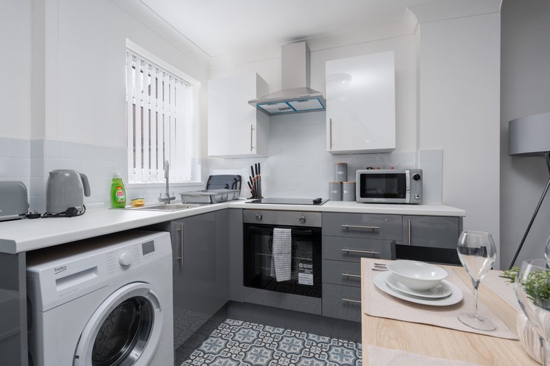 Modern kitchen with washing machine, dark cabinetry, white countertops and dining table