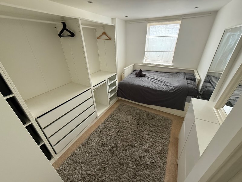 Small bedroom with single bed, open wardrobe, window, and grey carpet flooring