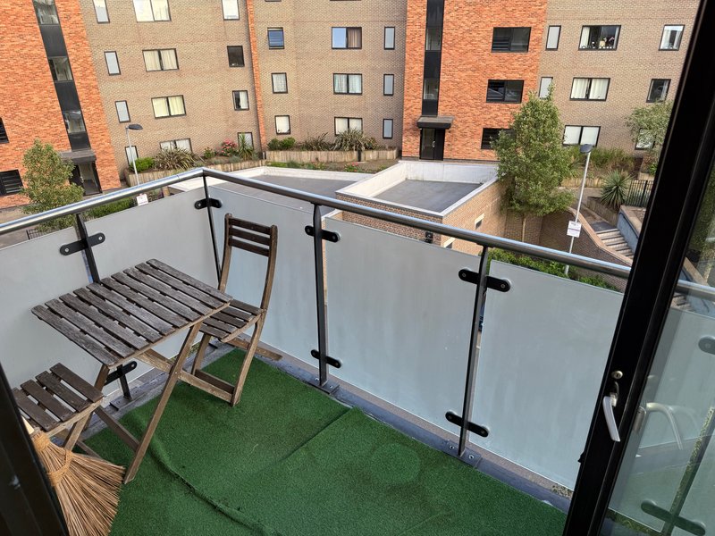 Modern balcony with synthetic grass, wooden loungers and glass railing overlooking courtyard