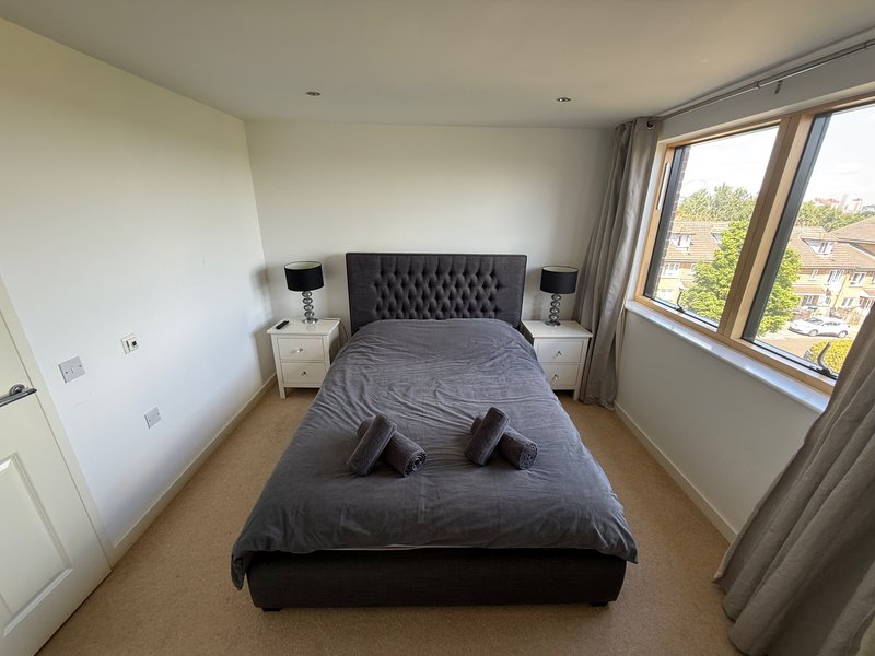 Modern bedroom with double bed, grey upholstered headboard, white nightstands and large window