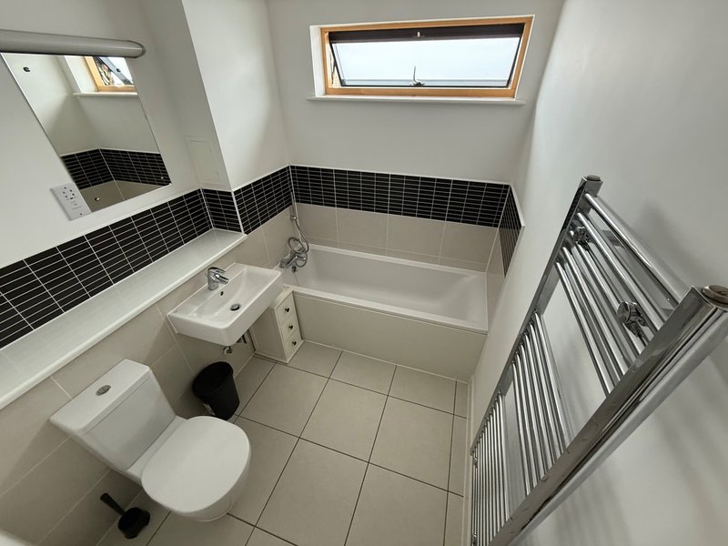 Modern bathroom with toilet, sink, bathtub, black tile accent wall and skylight