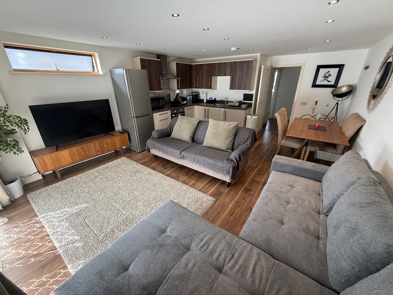 Open-plan living area with grey upholstered sofas, wooden TV stand, kitchen, dining table and hardwood flooring