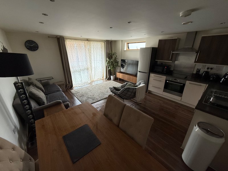Open-plan living room and kitchen with wooden flooring, sofa, dining table, and fitted appliances