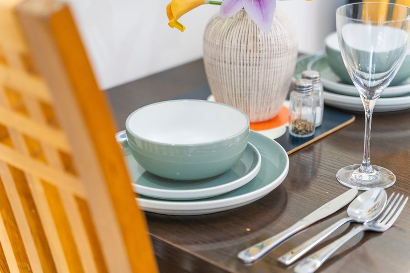 Dining table set with green bowls, white plates, glassware, cutlery and flower vase