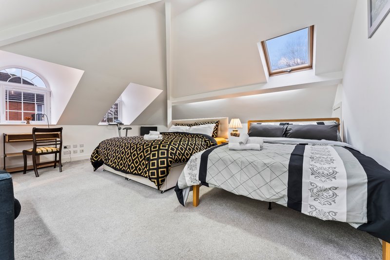 Bright attic bedroom with two beds, skylights, wooden desk and sloped ceiling