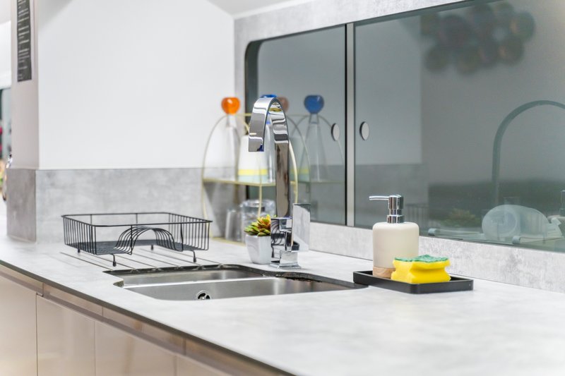 Modern kitchen sink with chrome faucet, white countertop, mirrored backsplash and bathroom accessories