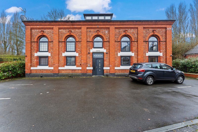 Red brick building exterior with arched windows, black door, and parked car in front