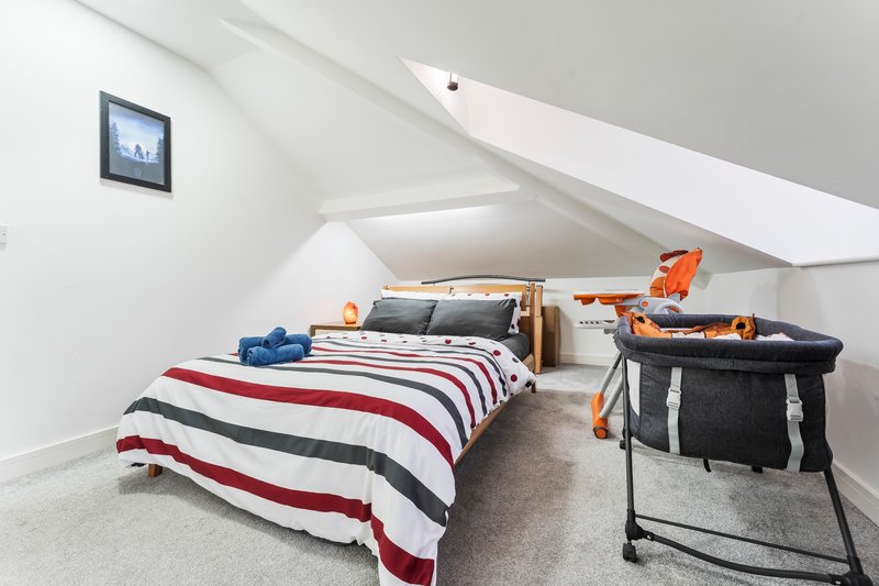 Attic bedroom with single bed, striped bedding, storage basket and skylight window